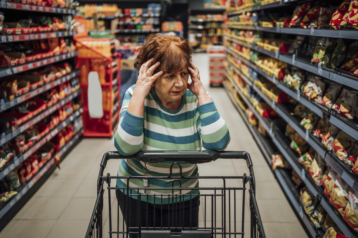 Elderly woman standing in the produce aisle at the supermarket feeling worried about the rising food prices
